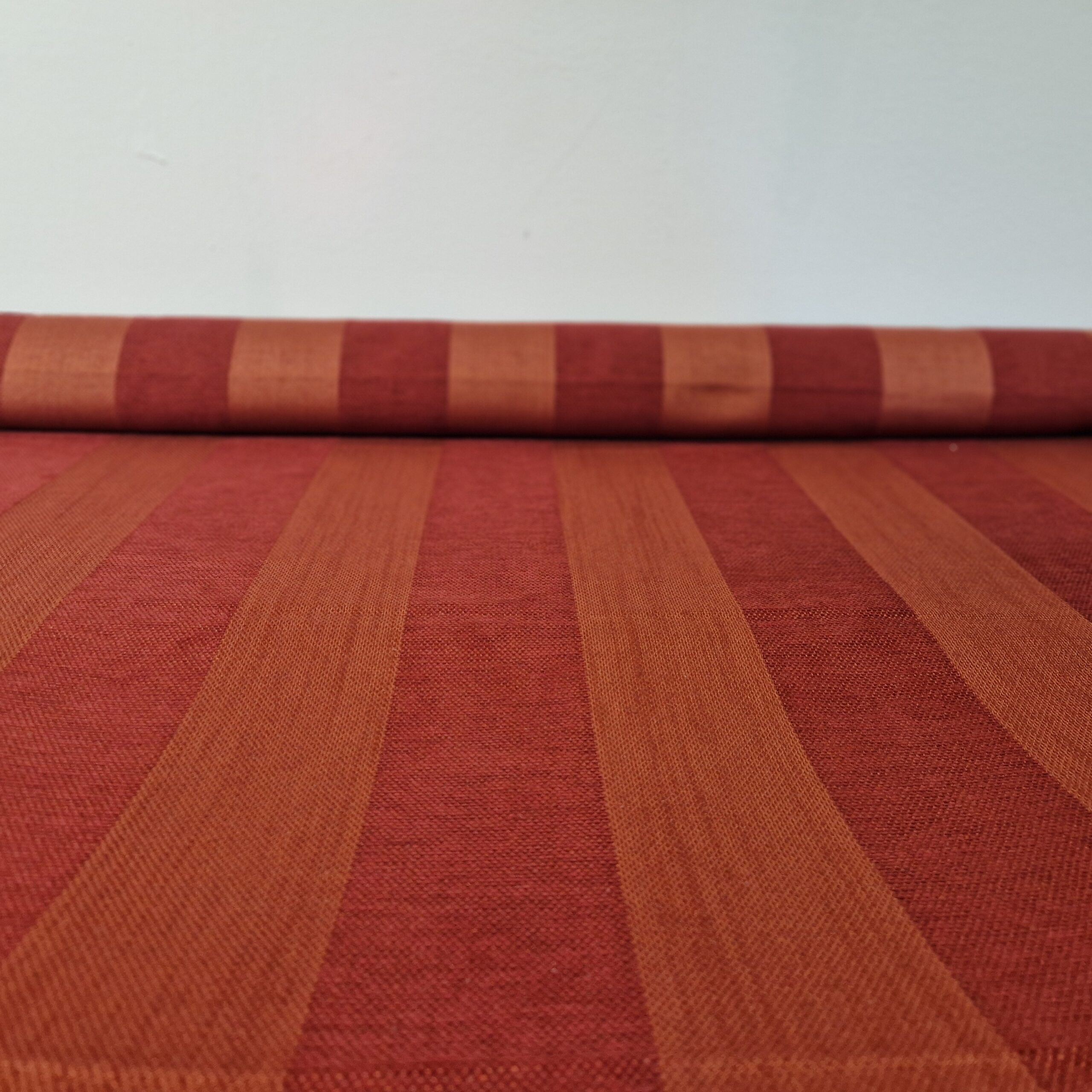 Gerollter Chenille Möbelstoff mit rot-terrakottafarbenem Streifenmuster.