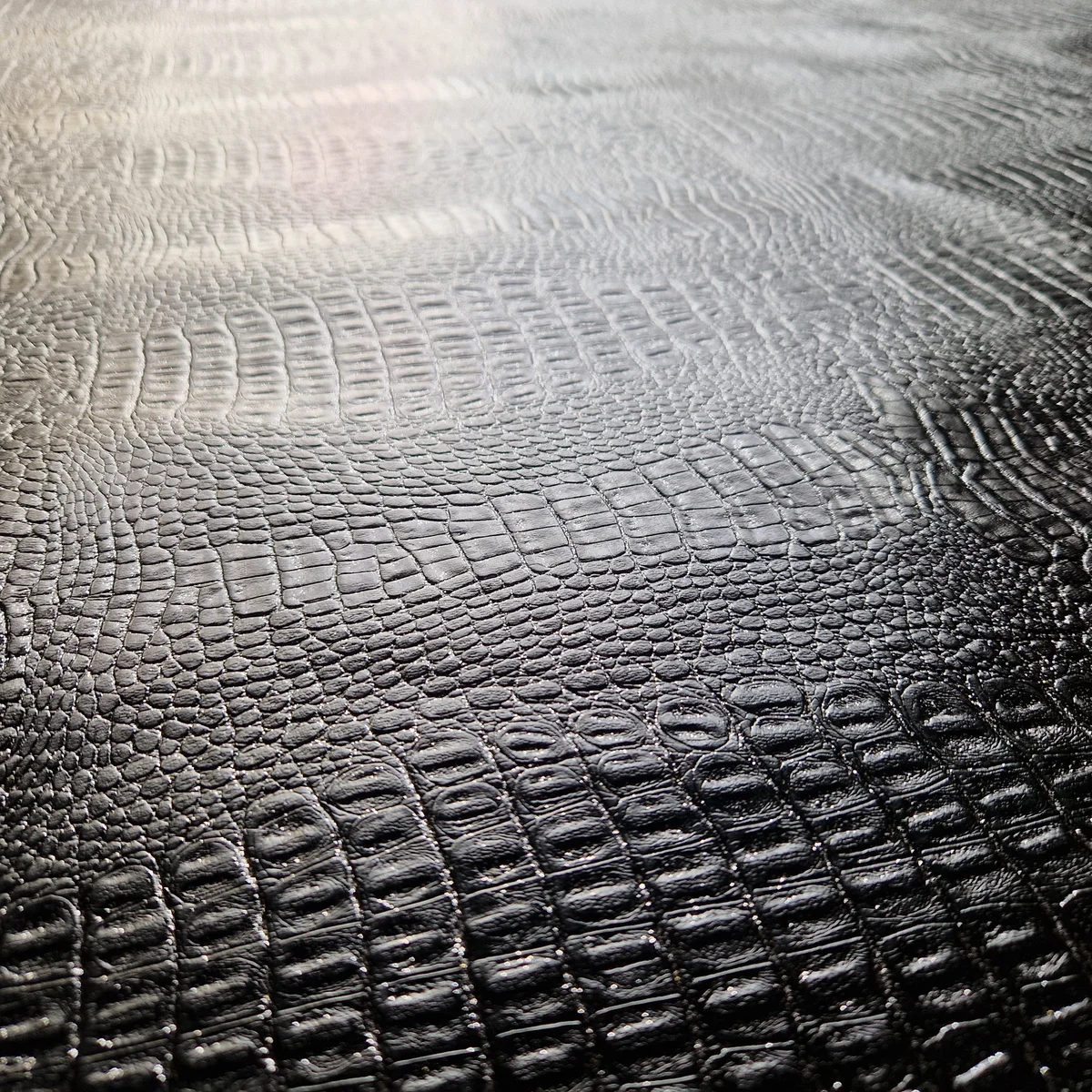 Detail der geprägten Echsenhaut auf schwarzem Kunstleder